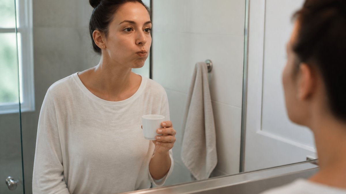 A person gently rinsing their mouth with a small cup of salt water in a bright bathroom, following dental implant aftercare instructions